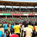 A vibrant, colorful scene of a South Sudanese football match in a local stadium, with enthusiastic fans cheering in the stands, showcasing the passion for football.